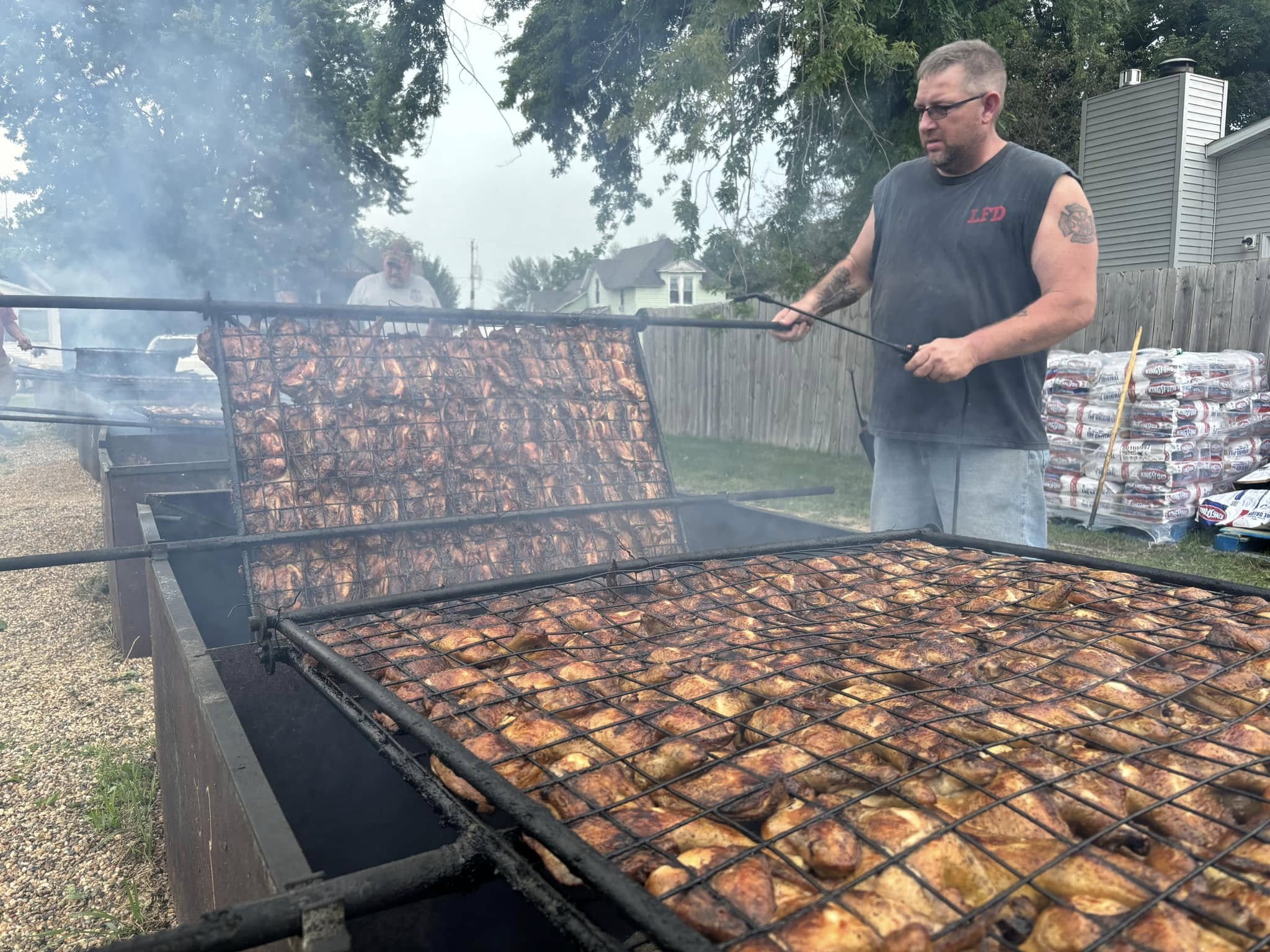 A man frying several dozen chickens on a large outside grill.